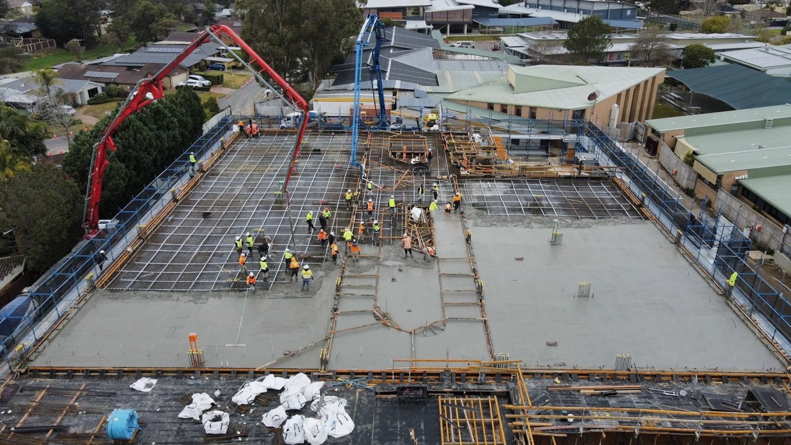 Twin boom pumps pouring suspended decks over a school campus, aerial view