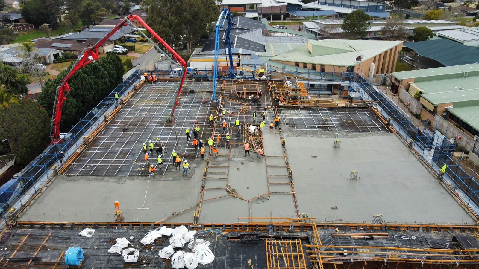 Twin boom pumps pouring suspended decks over a school campus, aerial view