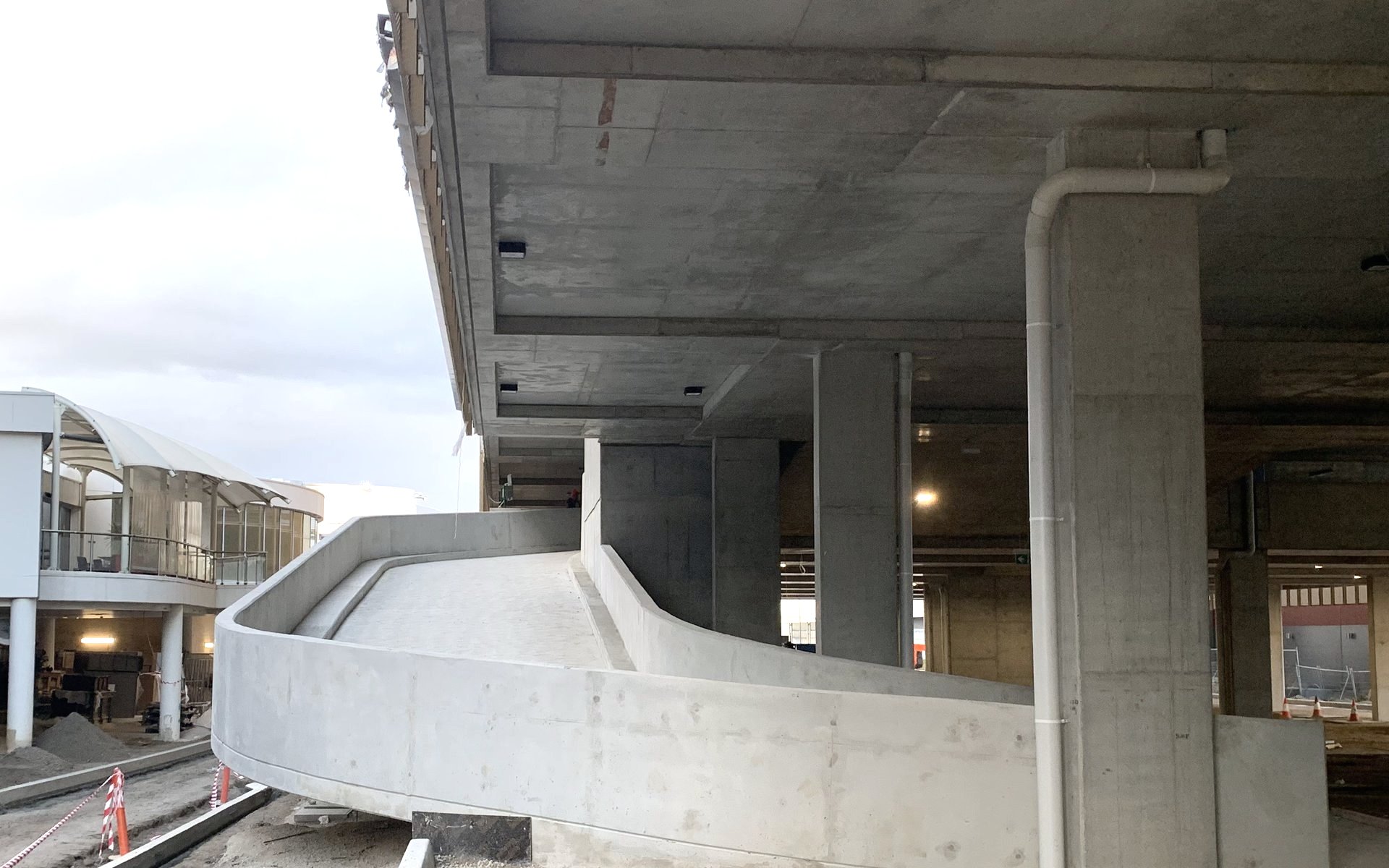 Curved off-form ramp wall sweeping beneath the suspended deck of a multi-level carpark under construction