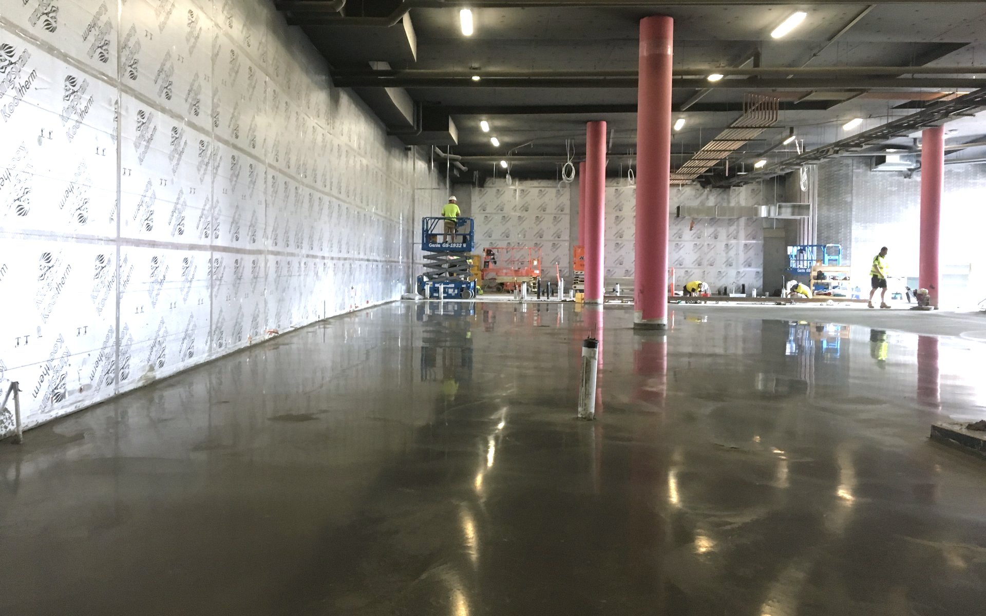 Freshly burnished coolroom slab inside insulated panel walls with crews finishing beyond