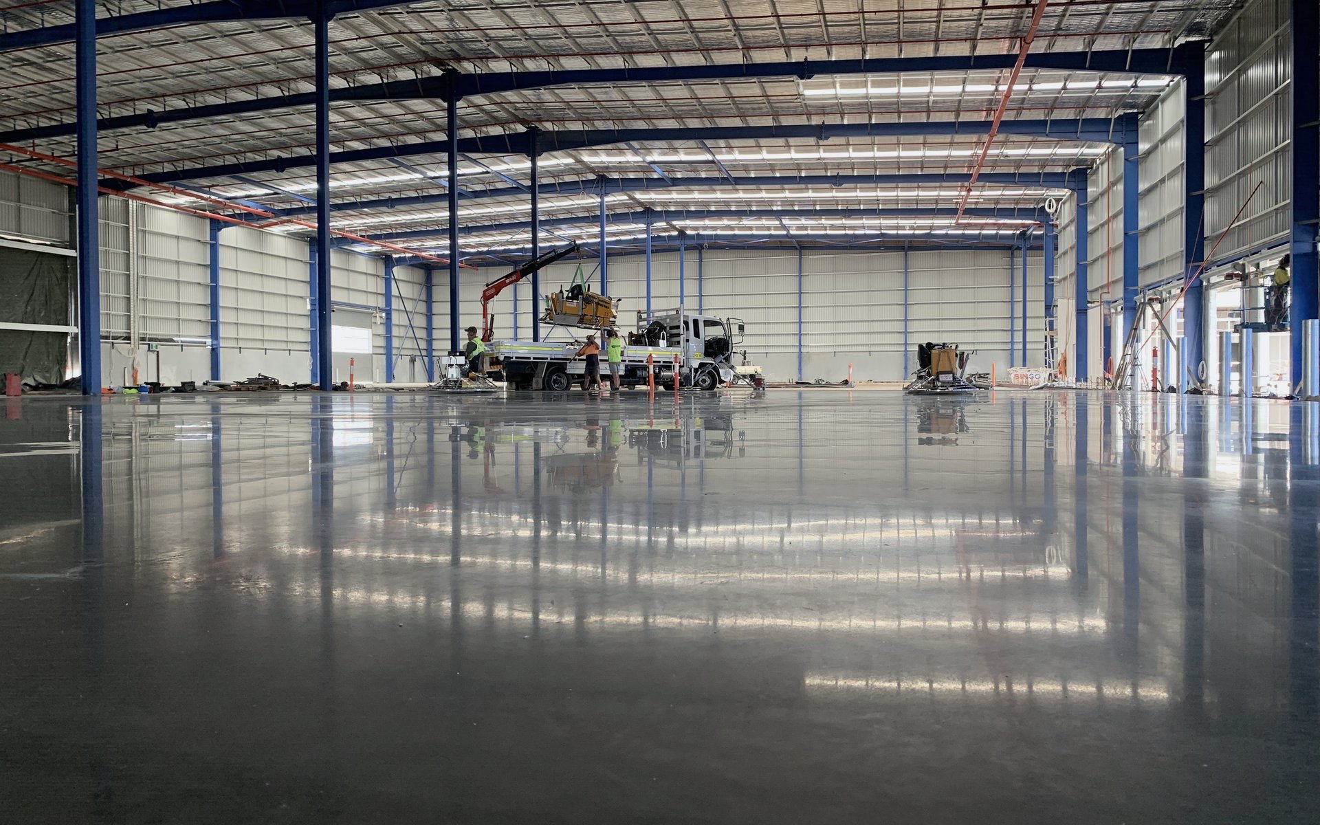 Burnished warehouse floor reflecting the portal frame after the final trowel pass