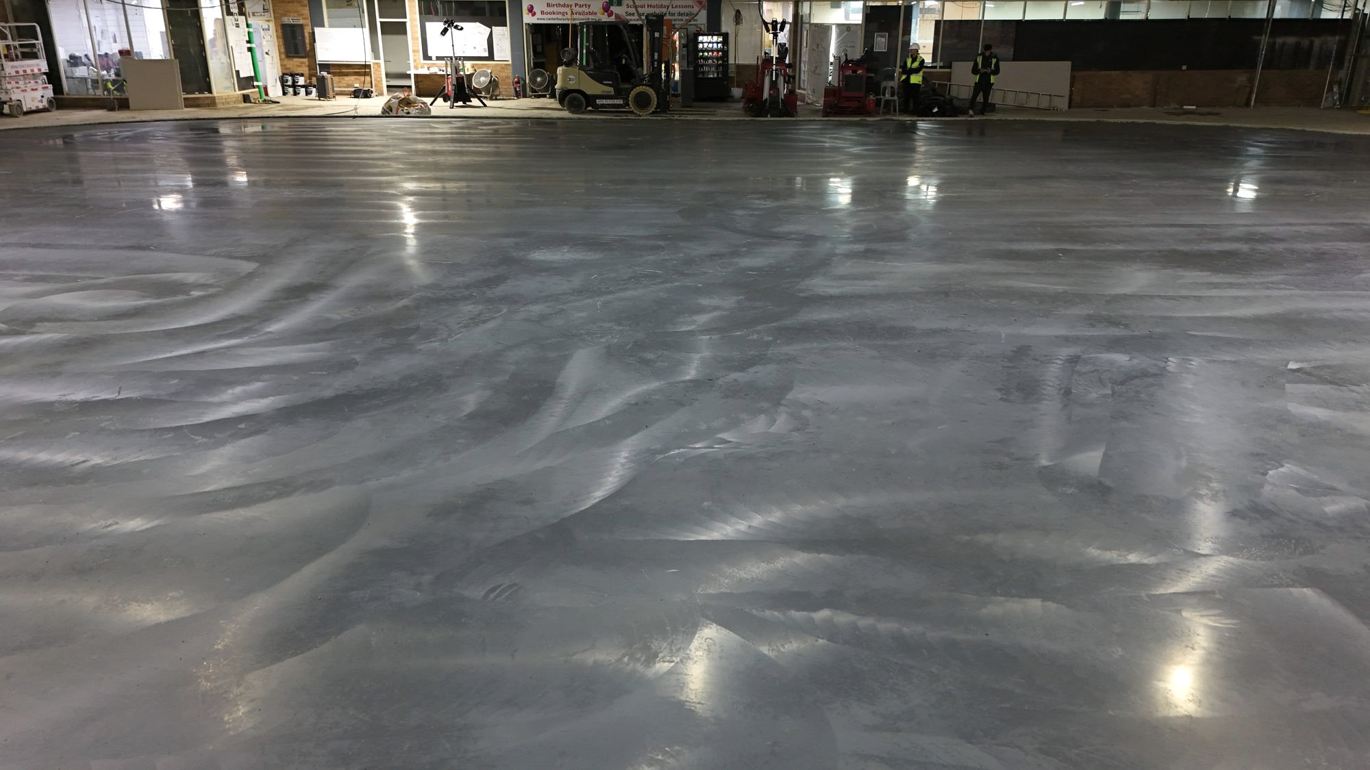 Machine-finished superflat competition ice rink slab under arena lights