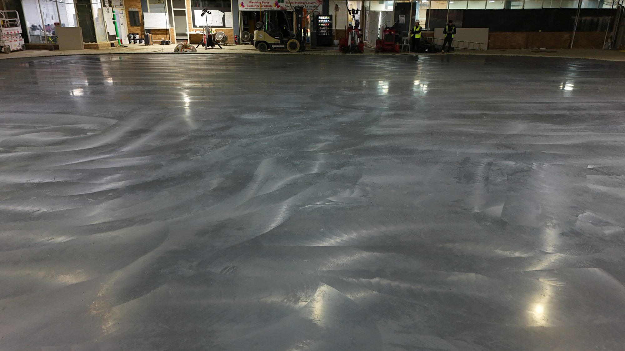 Machine-finished superflat competition ice rink slab under arena lights